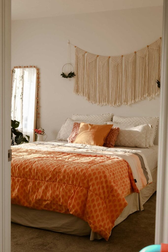 Cozy bedroom with macrame wall hanging and orange bedding.