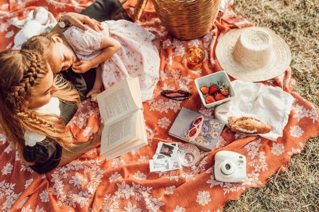 Mom reading a book to her daughter during a cozy picnic on a floral blanket.