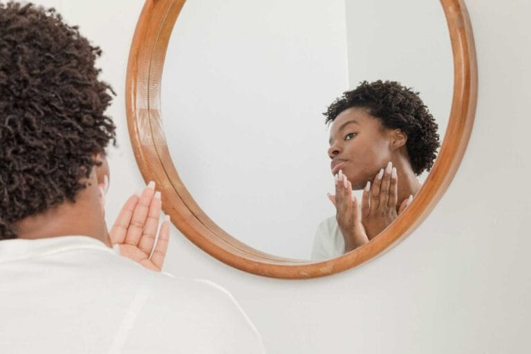 Woman applying AM skincare products while looking in a mirror.