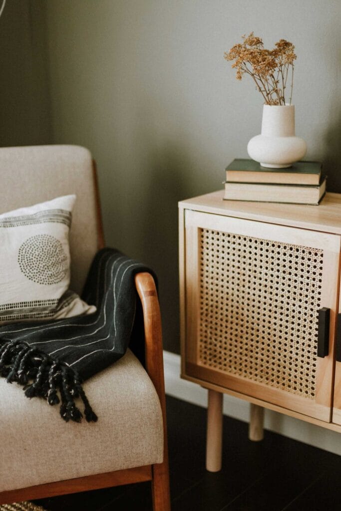 Cozy corner with an accent chair, throw blanket, and woven cabinet.