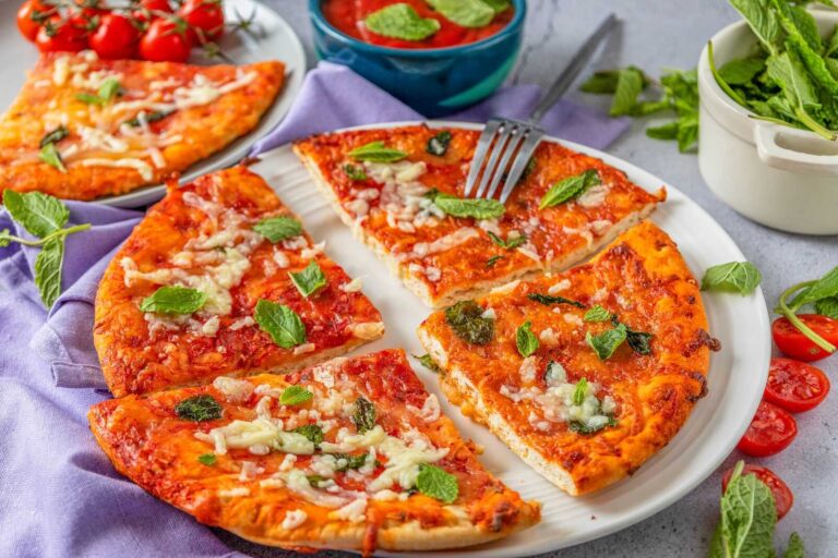 Homemade Margherita pizza slices with tomato sauce, melted mozzarella, and fresh mint on a white plate.