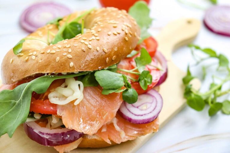 Smoked salmon bagel with tomato, red onion, greens, and melted cheese.