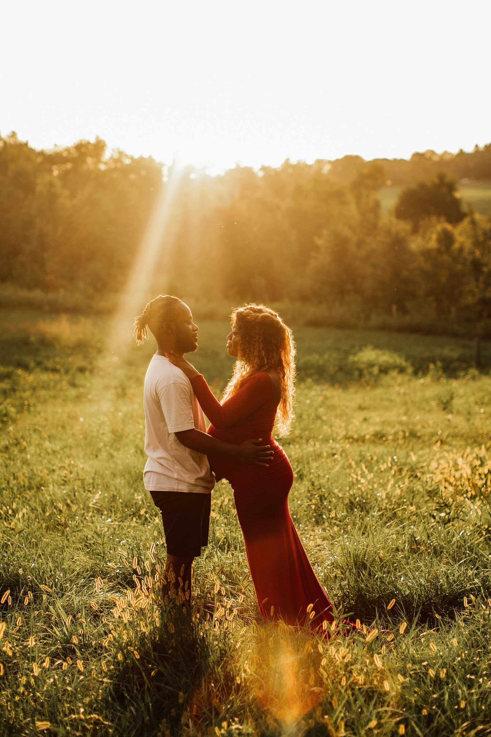 Couple embracing in golden field at sunset, romantic couples maternity photoshoot ideas outdoors.