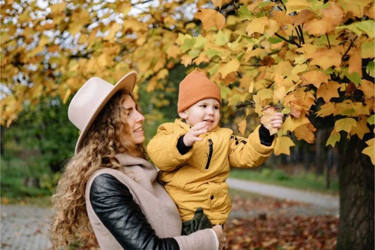 Mom holding toddler reaching for fall leaves, cozy fall family photoshoot outfit ideas.