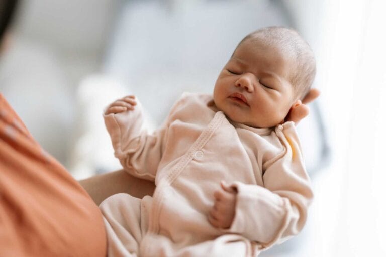 Newborn baby in a soft beige onesie sleeping in a parent’s arms during newborn fresh 48 photos.