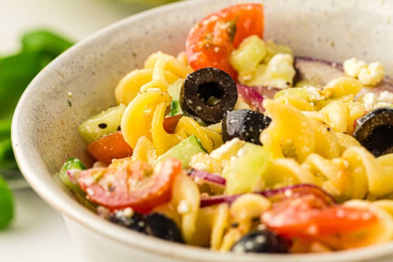 Close-up of Greek pasta salad with rotini pasta, cherry tomatoes, cucumbers, black olives, red onion, and feta cheese.
